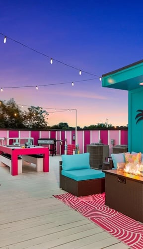 Rooftop deck at sunset with pink and teal decor, fire pit, and neon sign