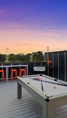 Rooftop deck at sunset with pool table, bar stools, and string lights