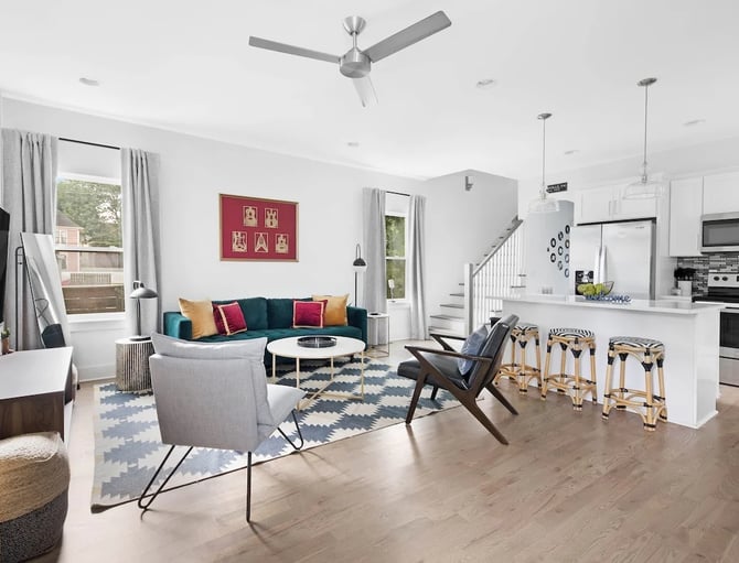 Open-plan living room and kitchen with teal sofa, gray armchairs, white kitchen island, and stainless steel appliances